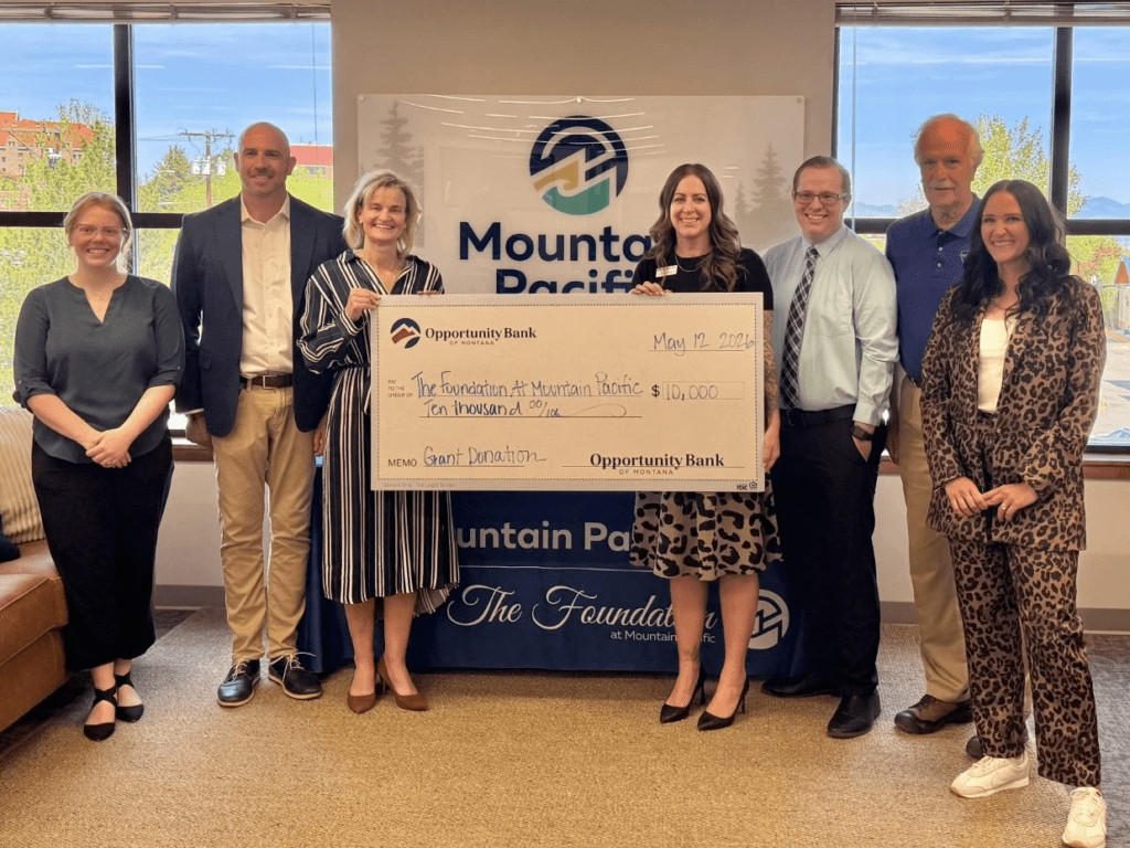 Seven people stand in an office, posing with a large ceremonial check from Opportunity Bank of Montana to The Foundation at Mountain Pacific, representing a ,000 grant donation.