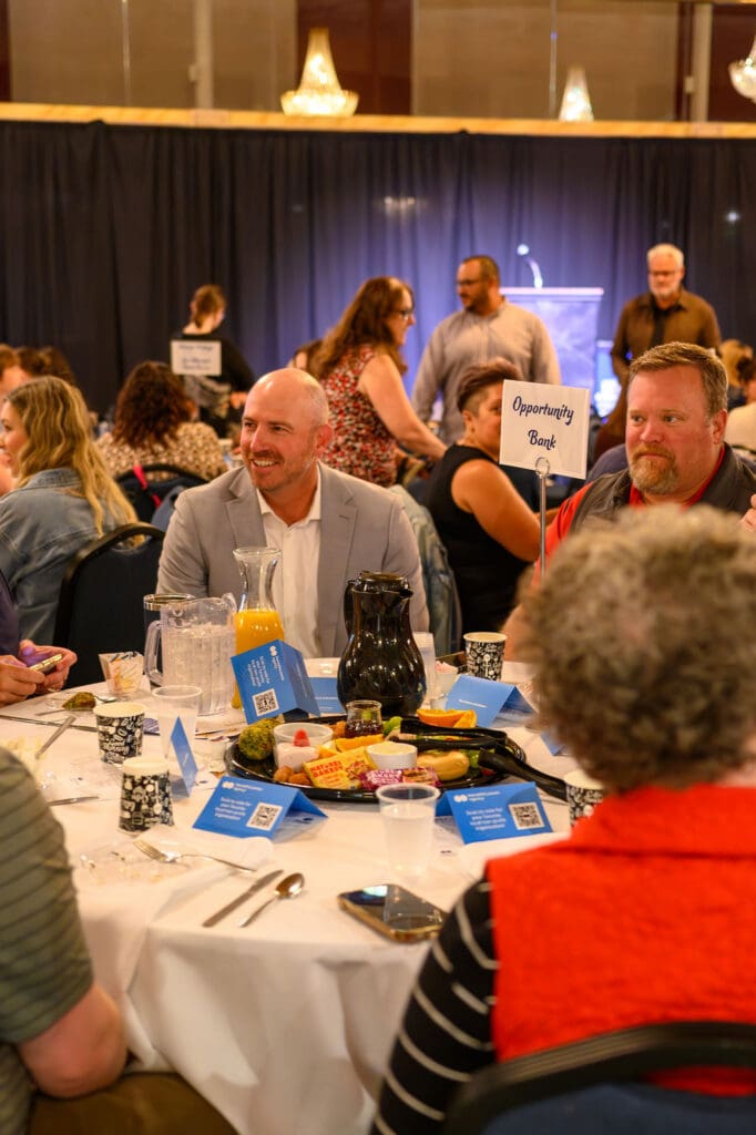 Guests seated at a round banquet table during a fundraiser, with an 'Opportunity Bank' sign visible in the background.